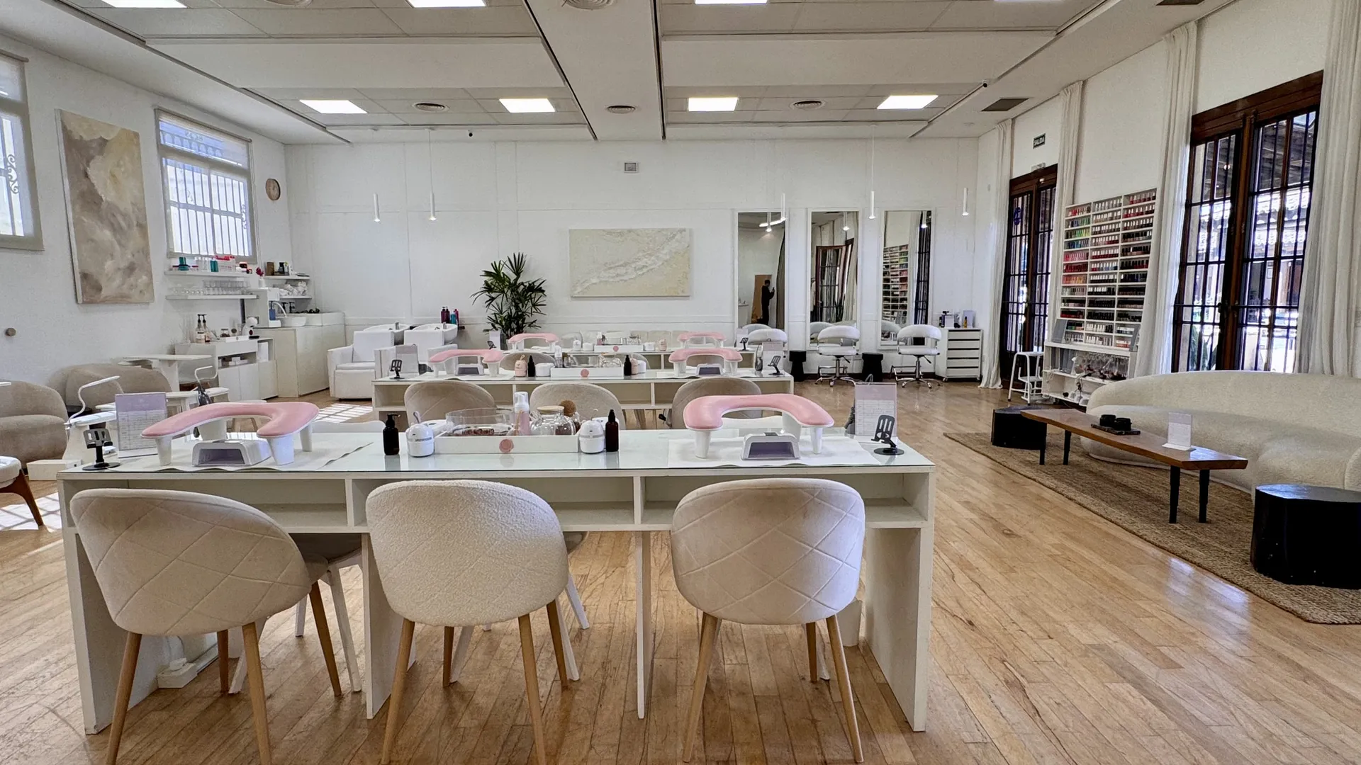 Salón de Sense Bene, con mesas de manicuría, espejos y un sector de espera junto a las ventanas.